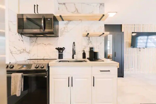 A modern kitchen with white cabinets, a built-in microwave, and a coffee machine.