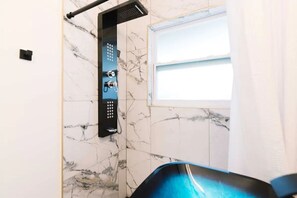Ein Badezimmer mit Dusche, Marmorwänden und einem Fenster.