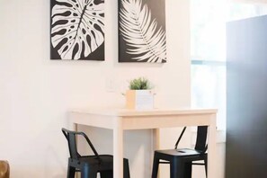 Ein Zimmer mit einem weißen Schreibtisch, zwei schwarzen Stühlen und zwei an der Wand befestigten Blätter-Kunstwerken.