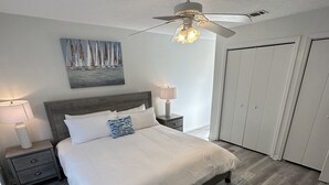 Un dormitorio con una cama, mesitas de noche, un ventilador de techo y un cuadro en la pared.
