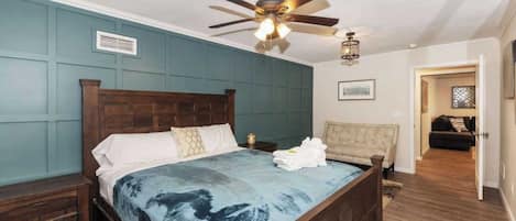 A bedroom with a large bed, wooden headboard, a ceiling fan, and a nightstand with a lamp.
