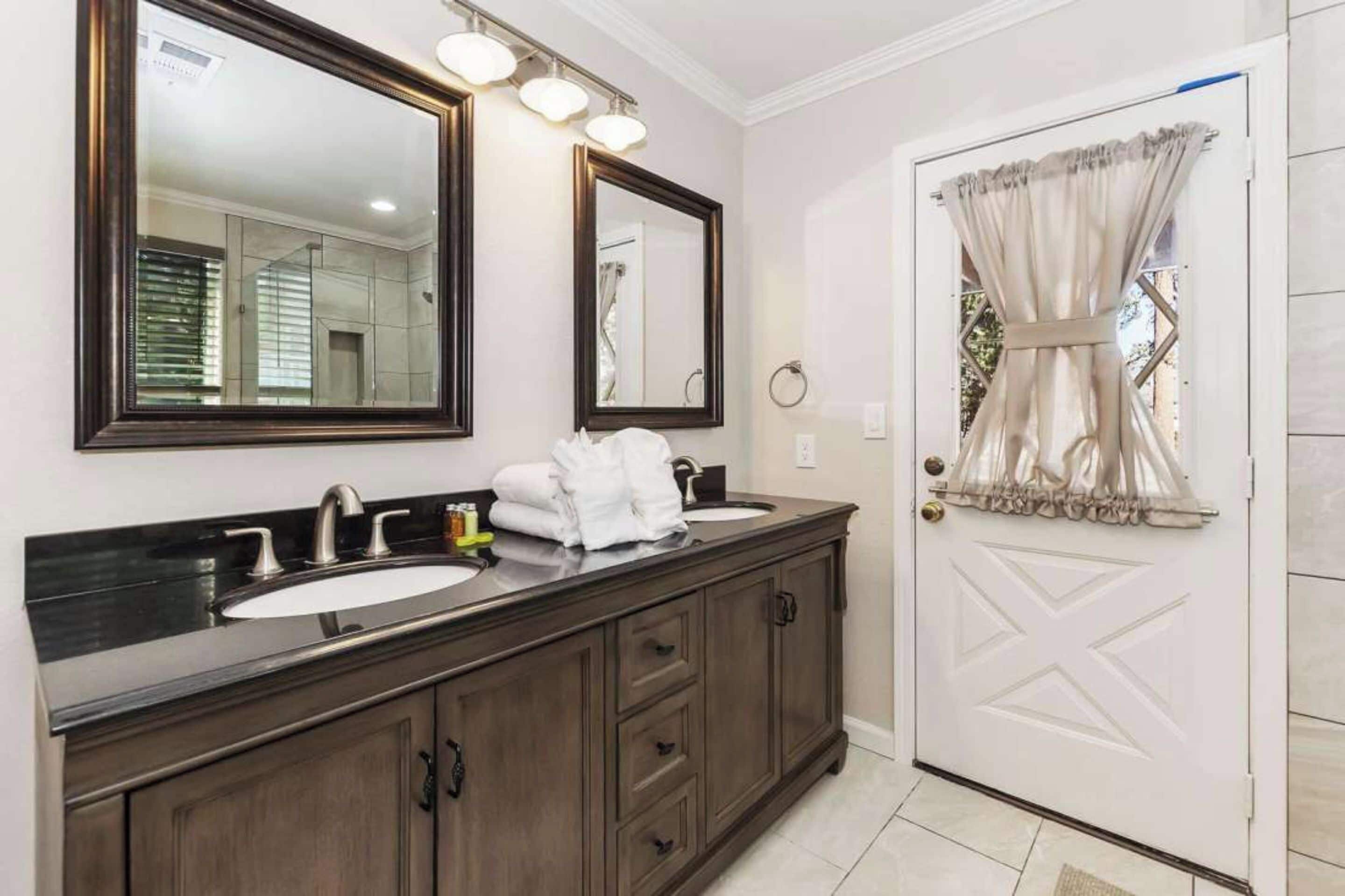 A bathroom with a double sink vanity, two mirrors, and a door with a curtain.