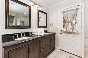 A bathroom with a double sink vanity, two mirrors, and a door with a curtain. - Walk to Lake! 7bdr, Hottub, Movie Theater, Gameroom Dawn and Dusk by Avantstay (Big Bear Lake)
