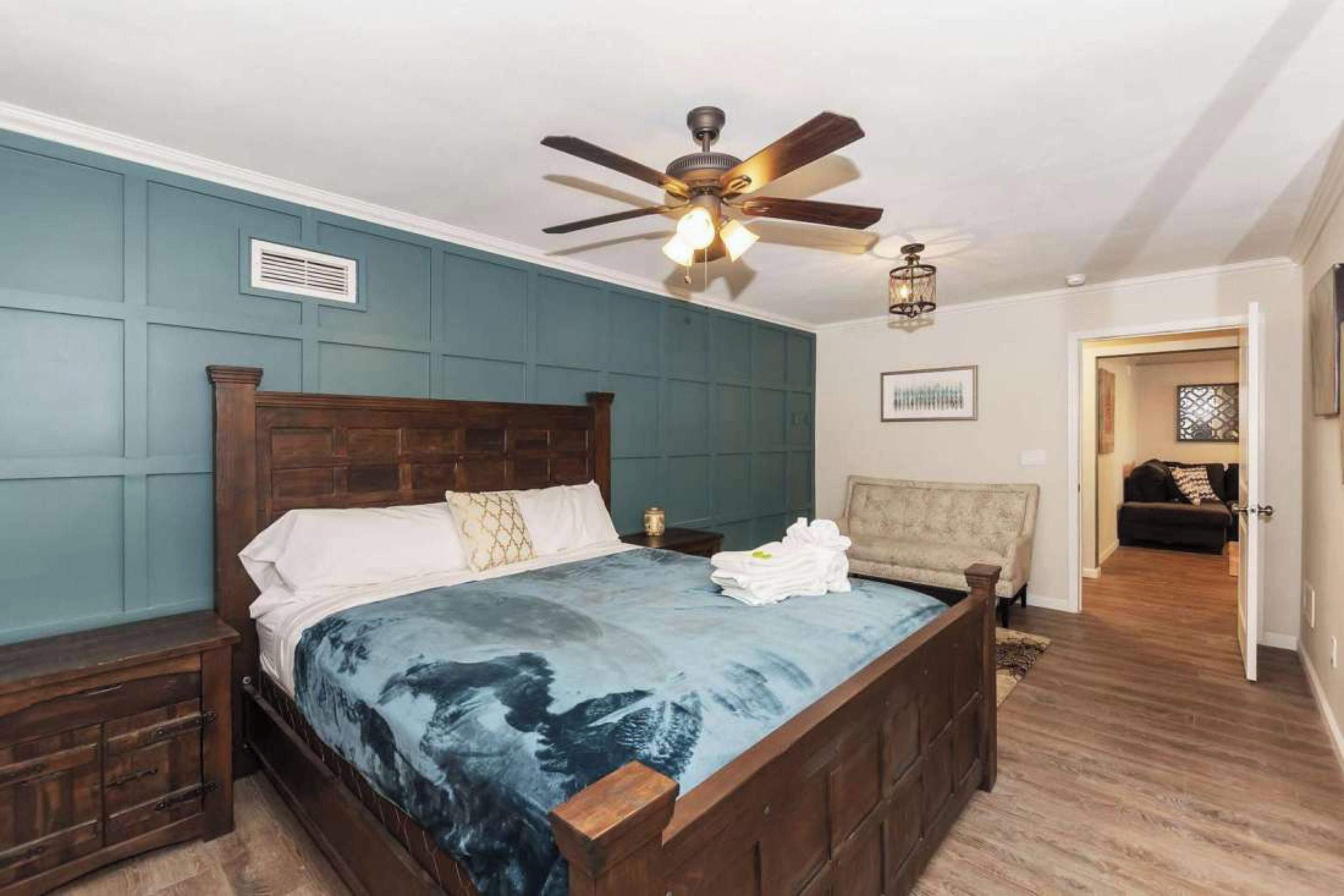 A bedroom with a wooden bed, a ceiling fan, a nightstand, and a chair.
