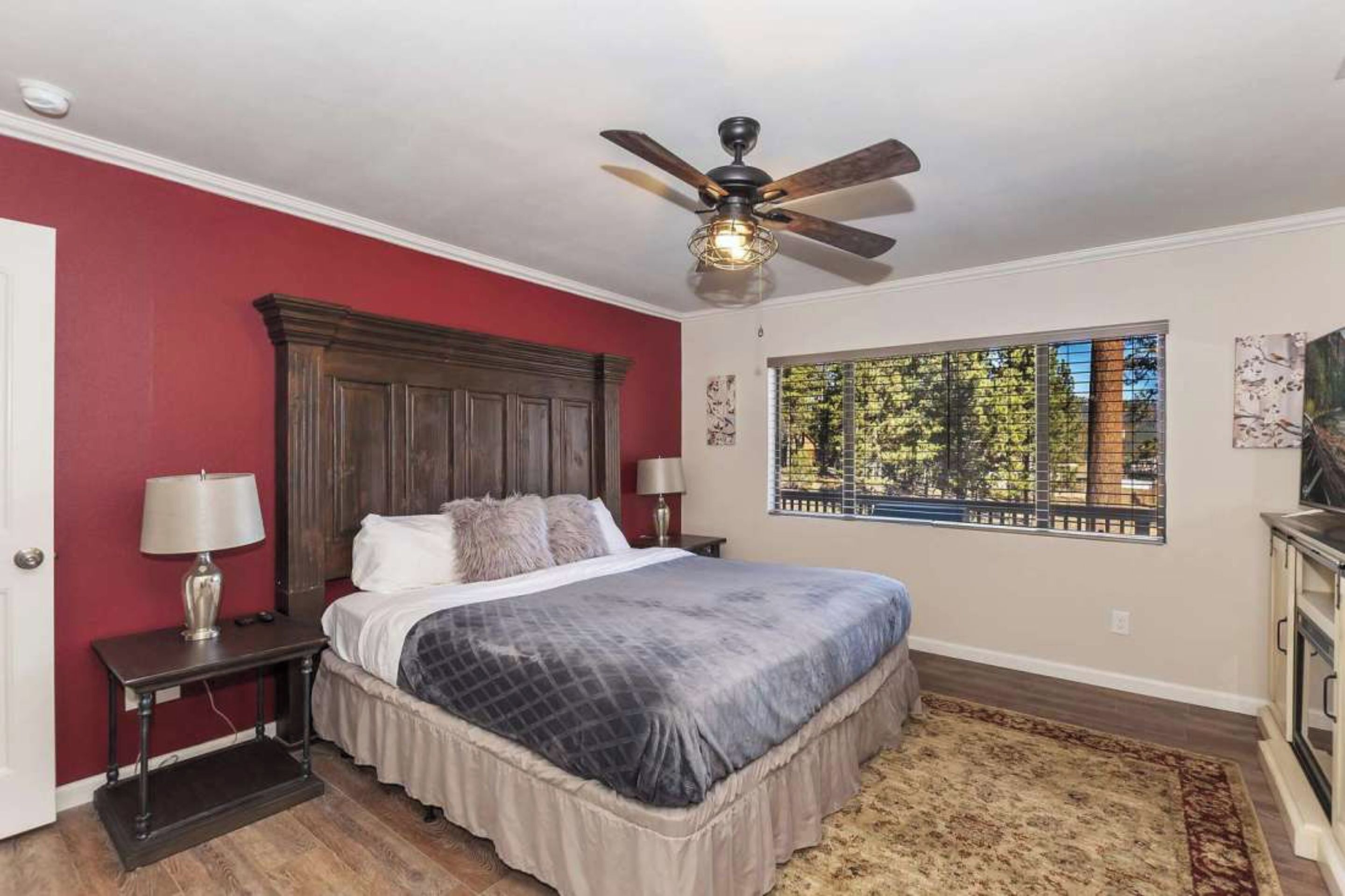 A bedroom with a bed, a ceiling fan, a window with a view, and a nightstand with a lamp.