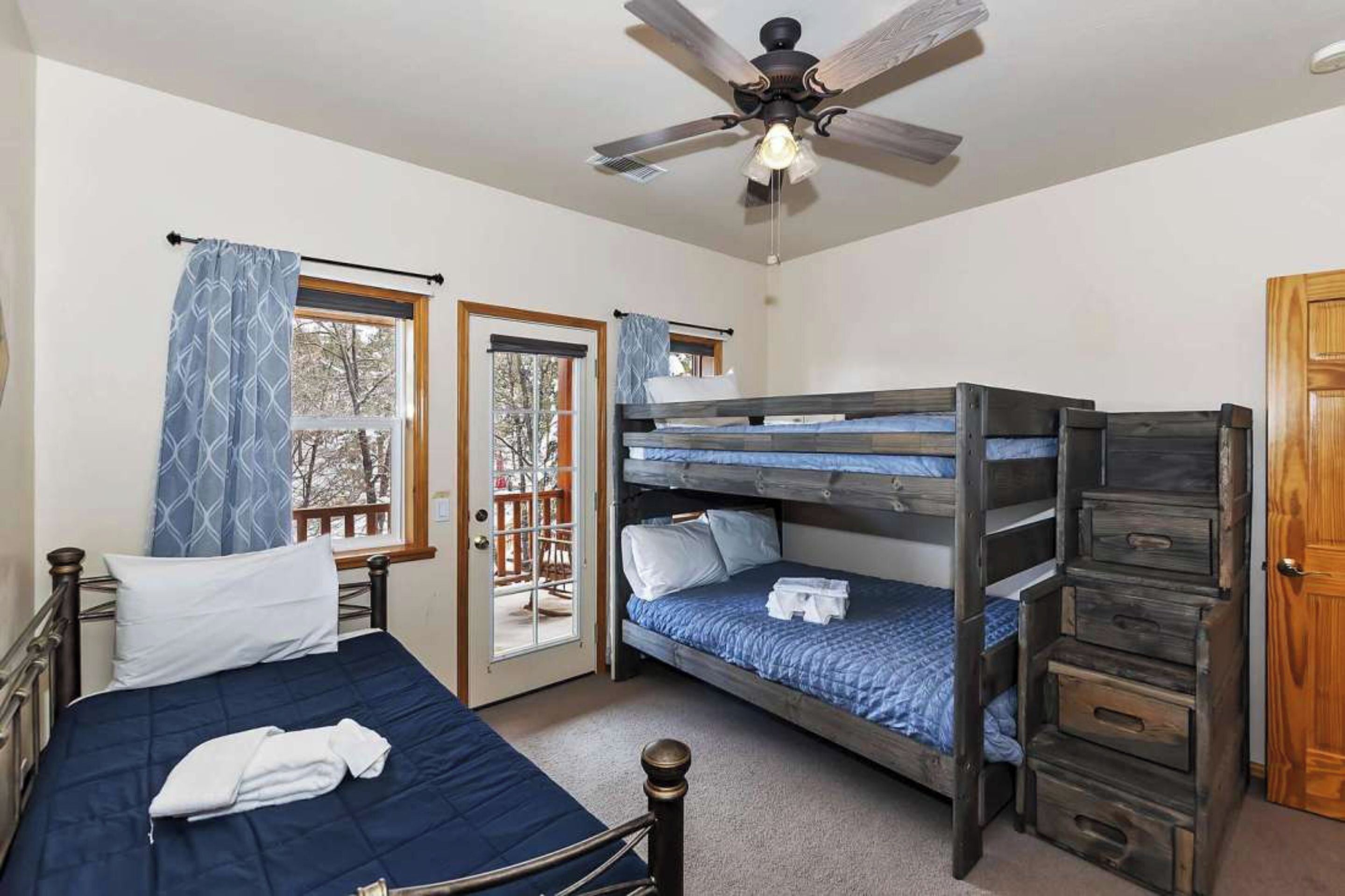 A room with a single bed, a bunk bed, a ceiling fan, and a door leading to an outdoor area.