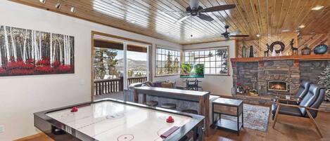 A spacious living room with a pool table, a fireplace, and a stone wall.