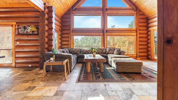 A log cabin interior with a large window, a sofa, a coffee table, and a rug.