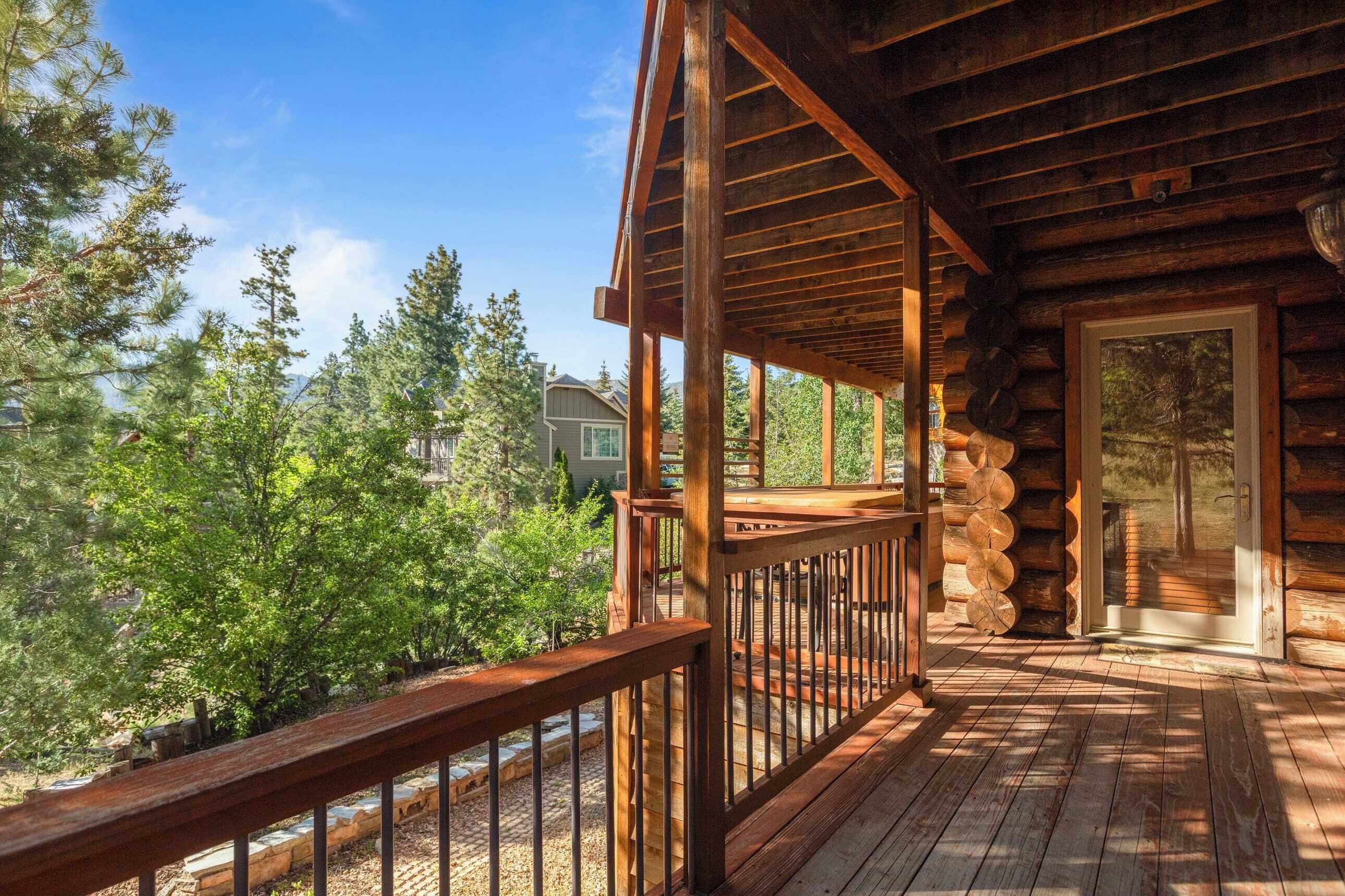 Une terrasse en bois avec une rambarde, entourée d’arbres et avec une maison en arrière-plan.