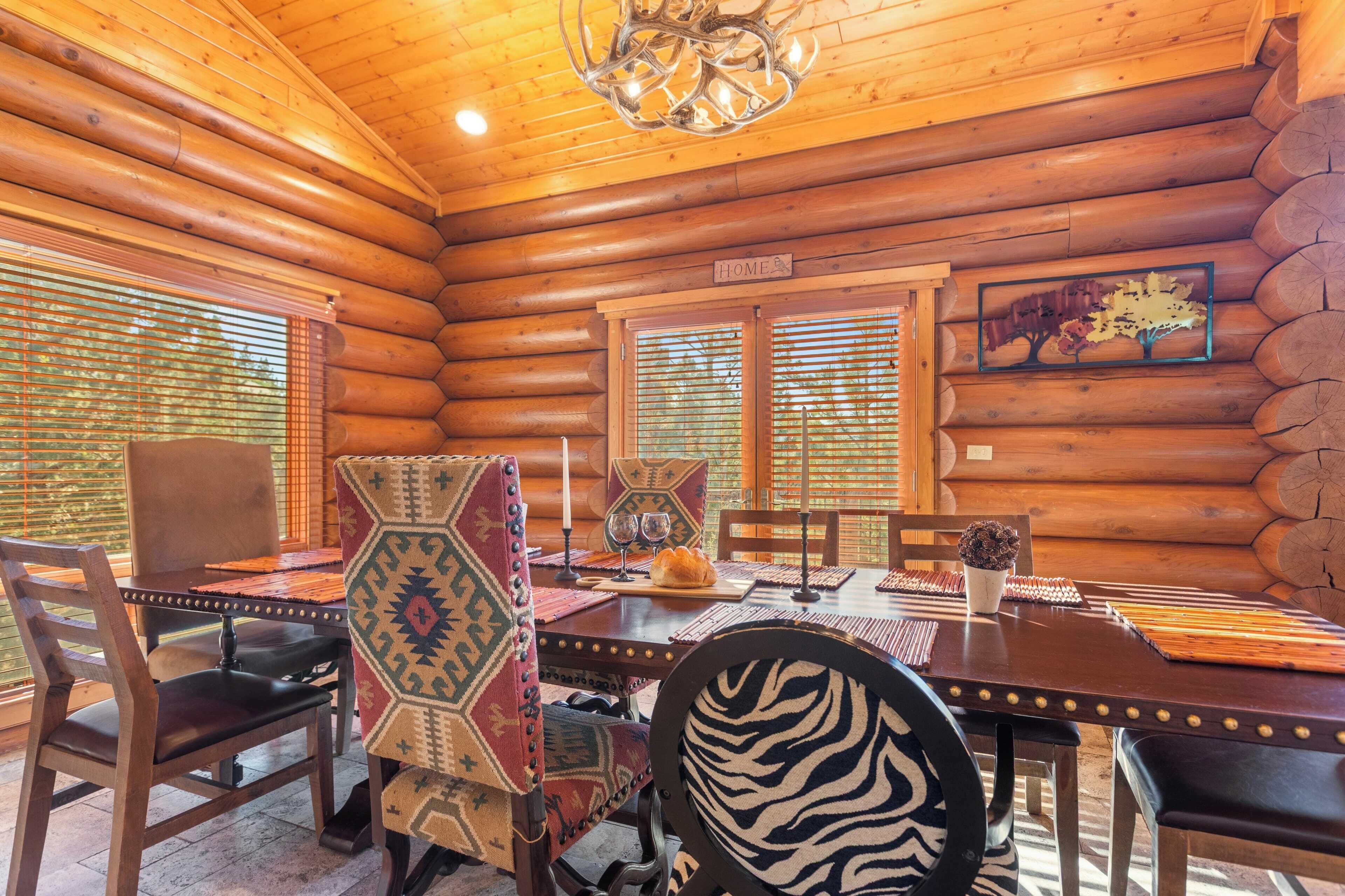 A log cabin interior with a wooden dining table, chairs, and a chandelier.