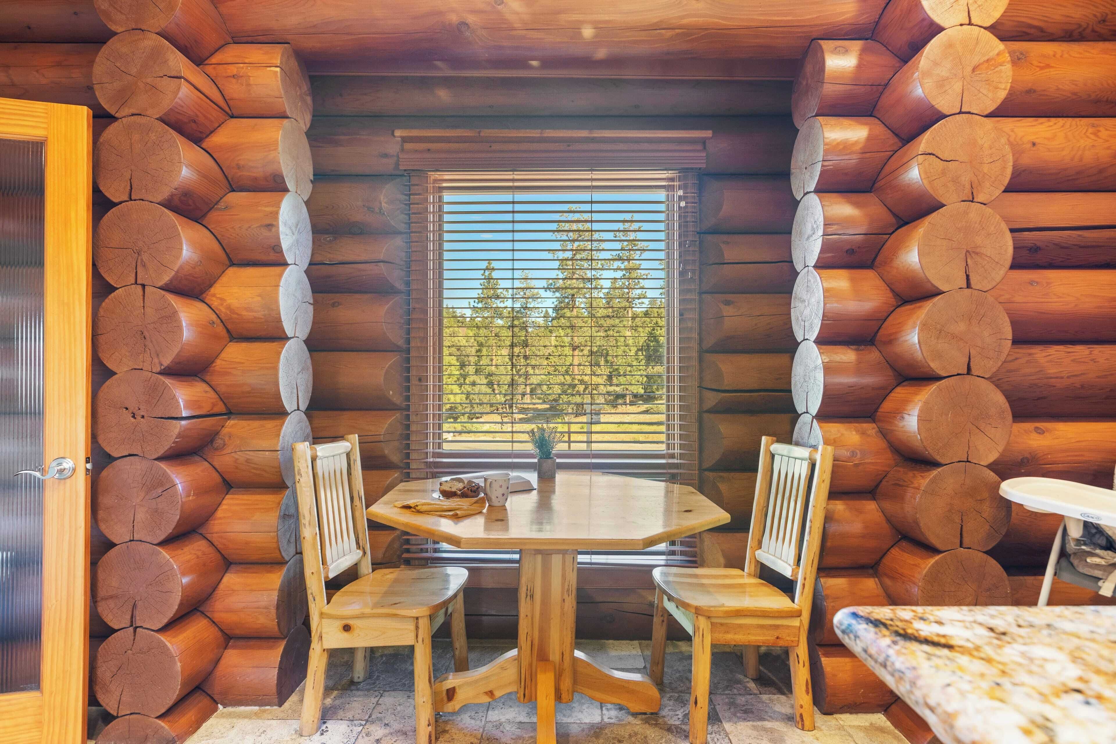 L’intérieur d’une cabane en rondins, avec une table et des chaises en bois, une fenêtre avec des stores et une porte.