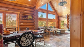 A log cabin interior with a dining area, a fireplace, and large windows. - 0.5mi to the Lake, Deck w/ Views, Poker Table Eagle Ridge Retreat by Avantstay (Big Bear Lake)