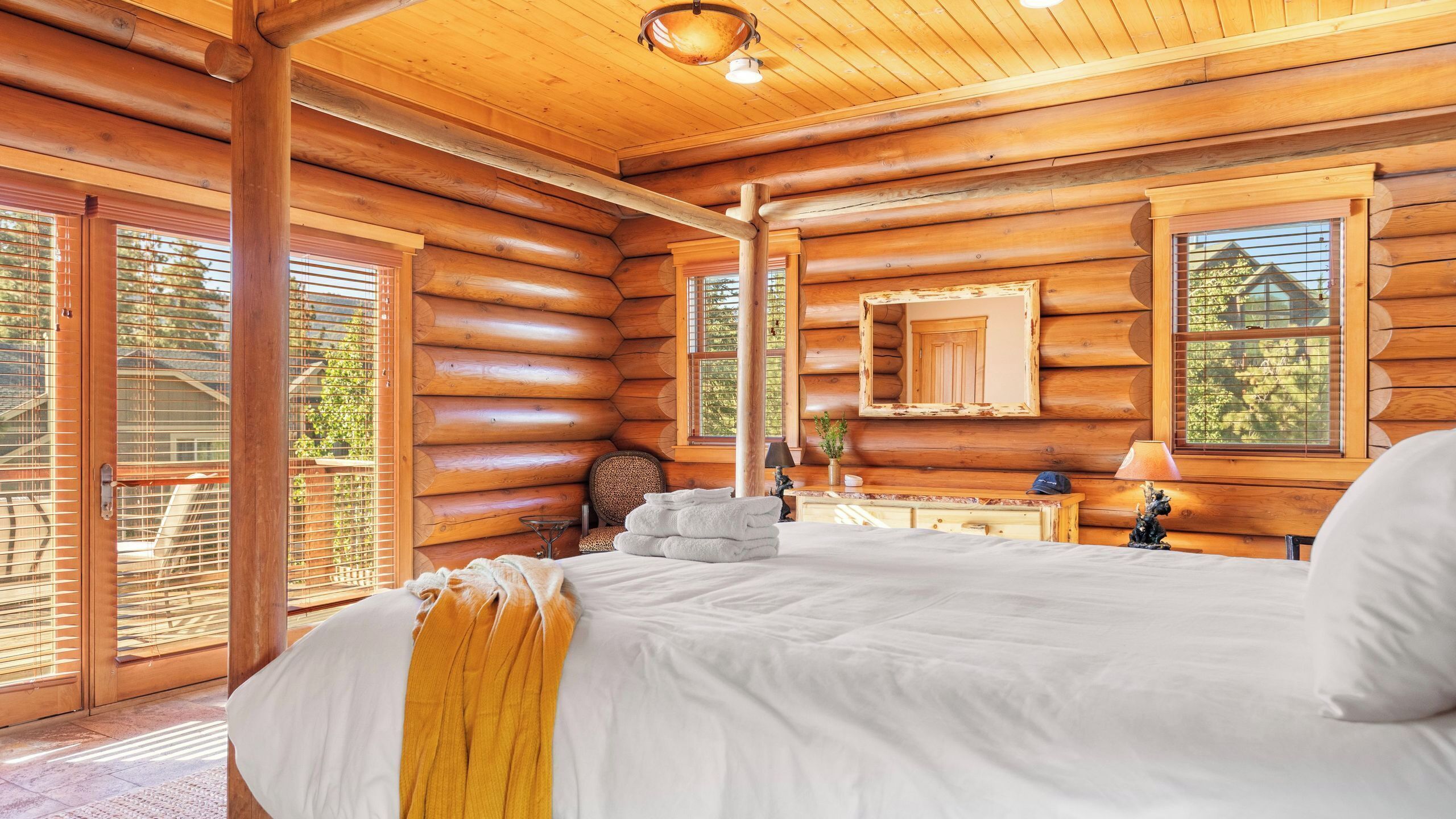 Ein Schlafzimmer in einer Blockhütte mit Bett, Spiegel und Fenster mit Blick auf Bäume.