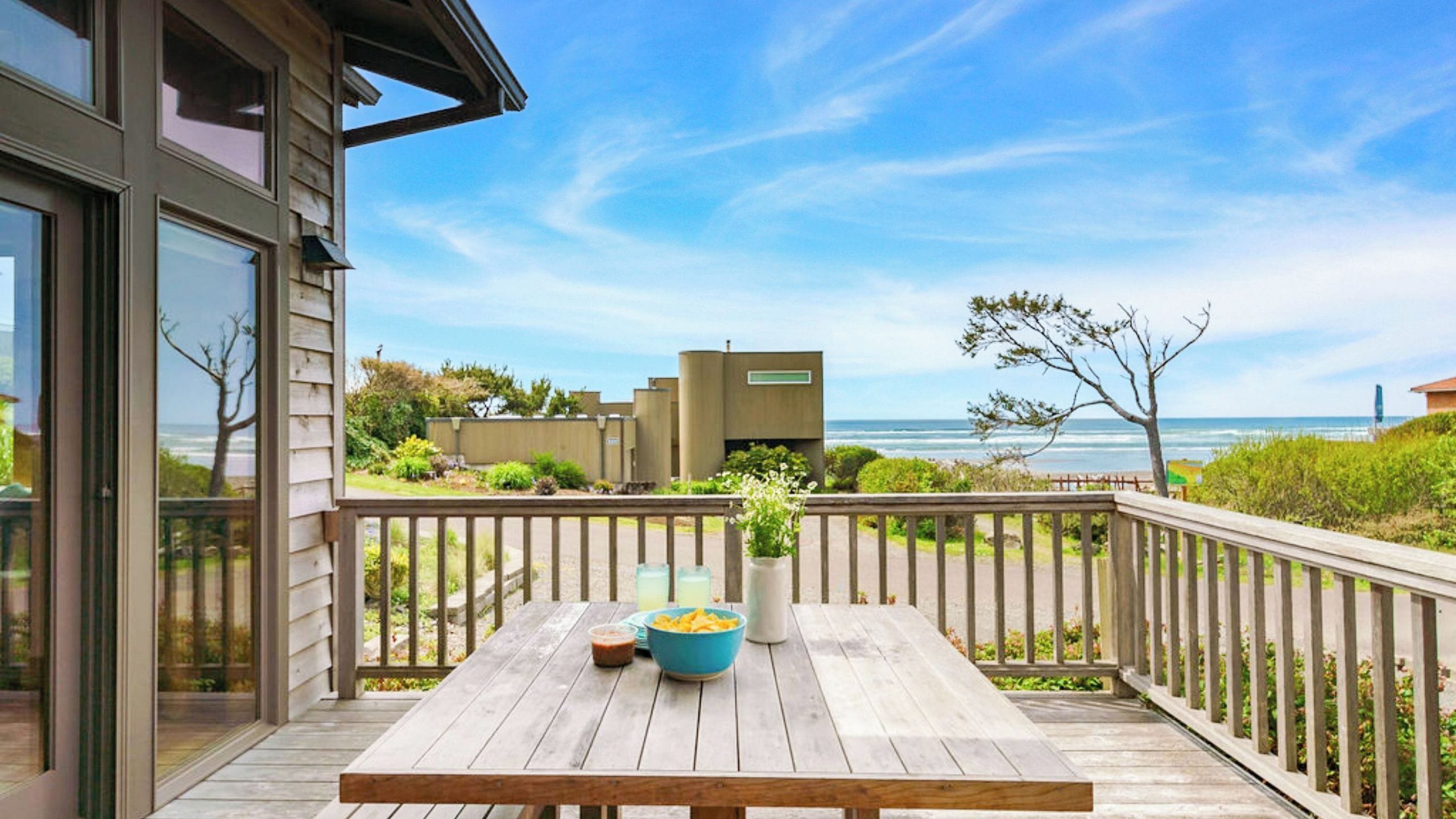A wooden deck with a table, a bowl of chips, and a vase with flowers.