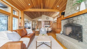 A spacious living room with a wooden ceiling, a stone fireplace, and a leather sofa. - The Castle Rock Estate by Avantstay Steps From Arch Cape Beach w/ Hot Tub & Sauna (Arch Cape)