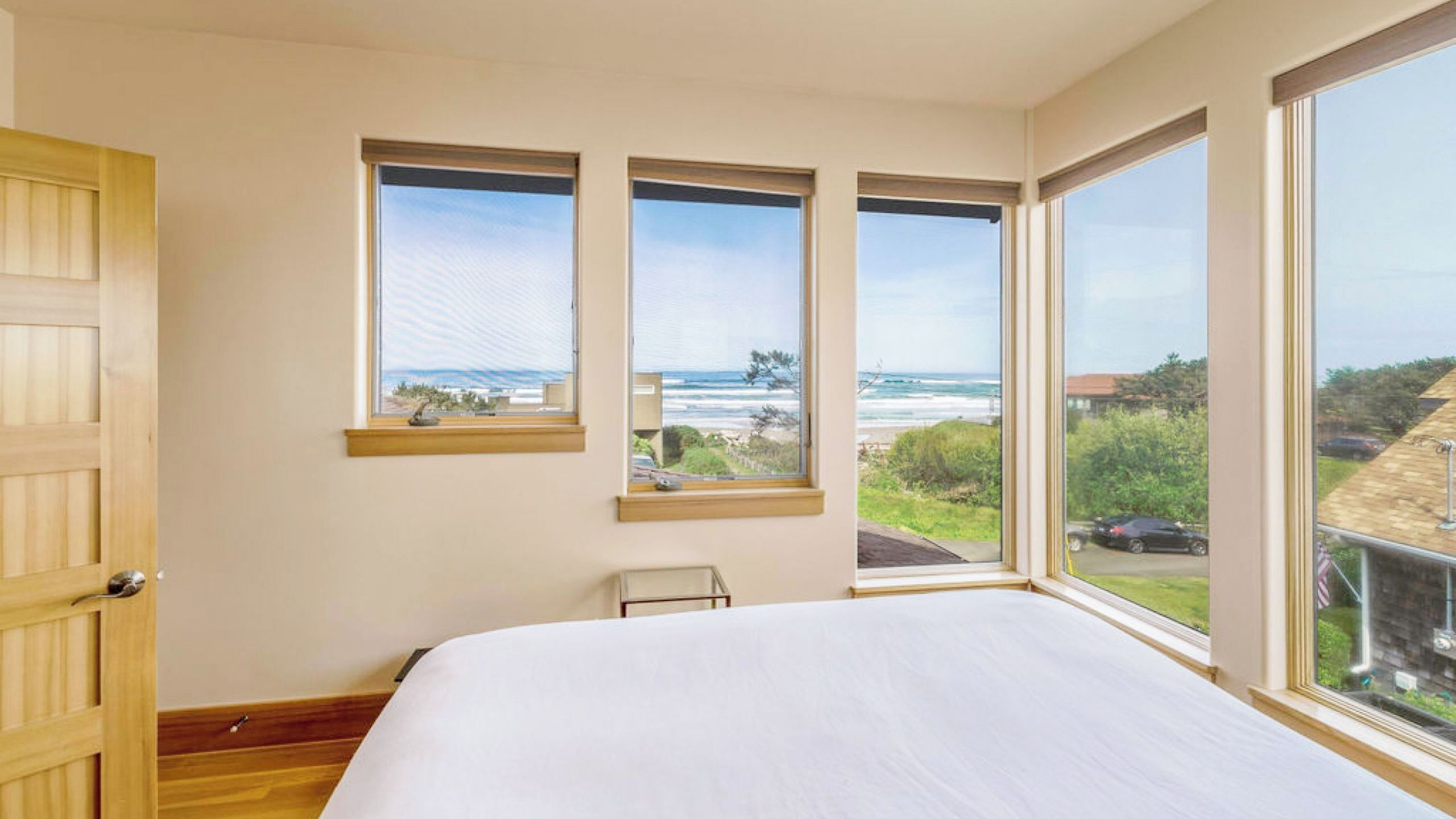 A bedroom with a large bed, three windows, and a view of the ocean.