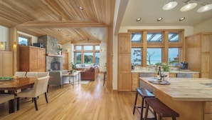 A spacious kitchen with wooden cabinets, a large island, and a stone fireplace. - The Castle Rock Estate by Avantstay Steps From Arch Cape Beach w/ Hot Tub & Sauna (Arch Cape)