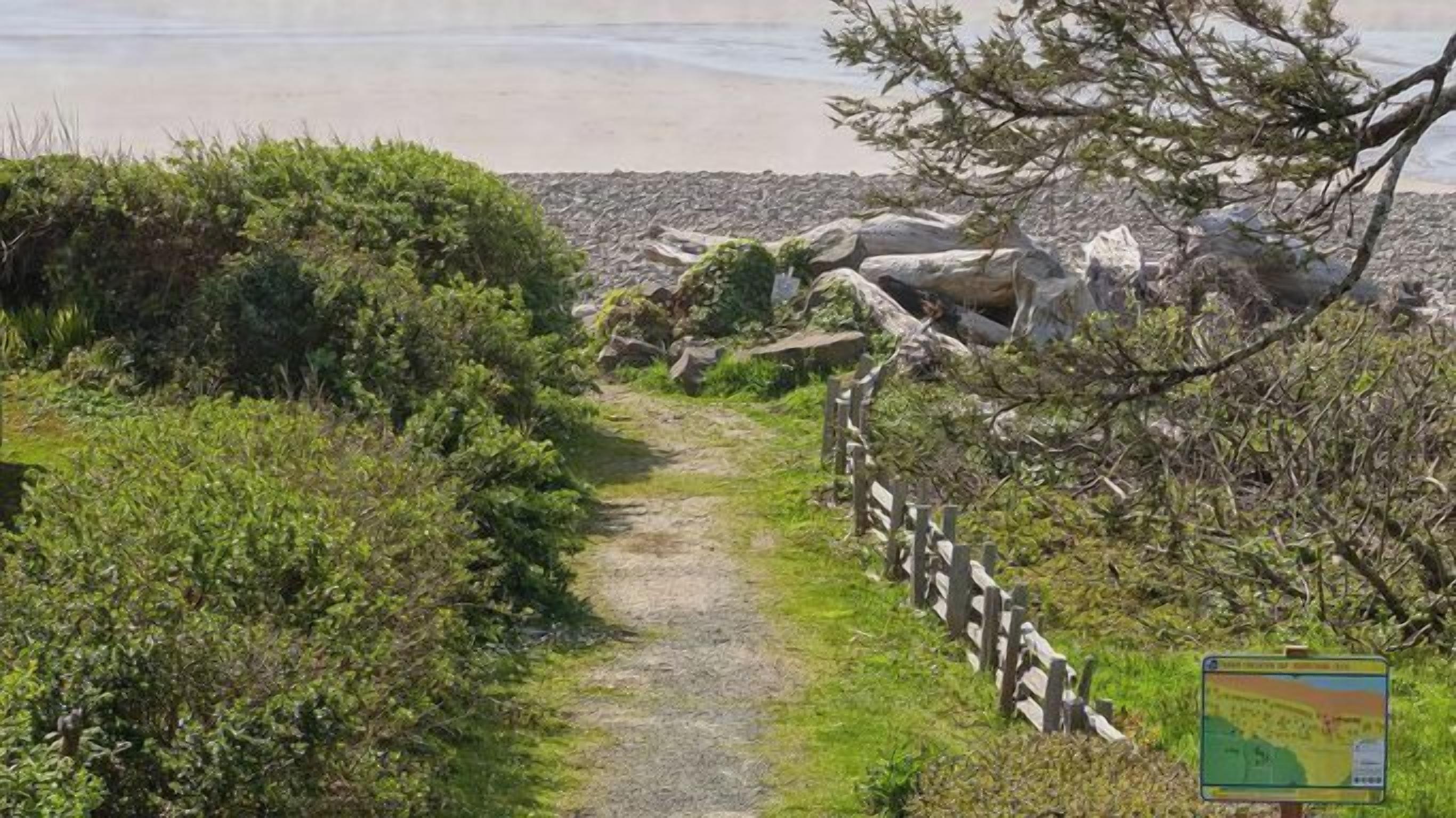 A pathway leading to a beach with a wooden fence and a signboard.
