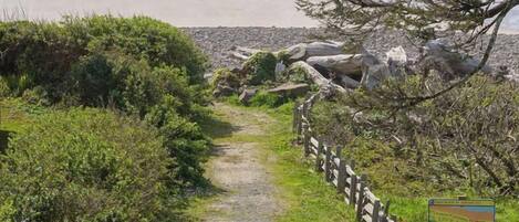 A pathway leading to a beach with a wooden fence and a signboard.