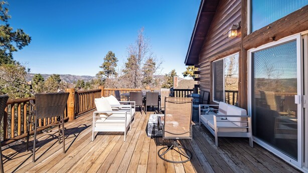 Une terrasse en bois avec des meubles d’extérieur, une grande porte-fenêtre coulissante et une vue sur le paysage environnant.