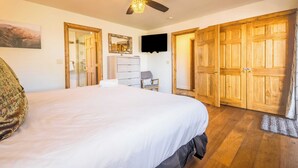 Une chambre avec un grand lit, un ventilateur de plafond, une télévision, des armoires en bois et un miroir.