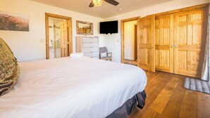 Une chambre avec un grand lit, un ventilateur de plafond, une télévision, des armoires en bois et un miroir au mur.