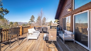 Une terrasse en bois, aménagée avec du mobilier d’extérieur, notamment des chaises et un canapé, qui offre une vue sur un paysage montagneux.