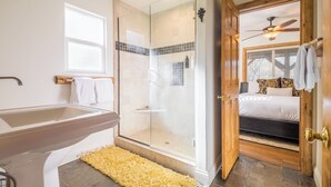 Une salle de bain dotée d’une douche à parois de verre, d’une baignoire et d’une porte en bois donnant sur une chambre.