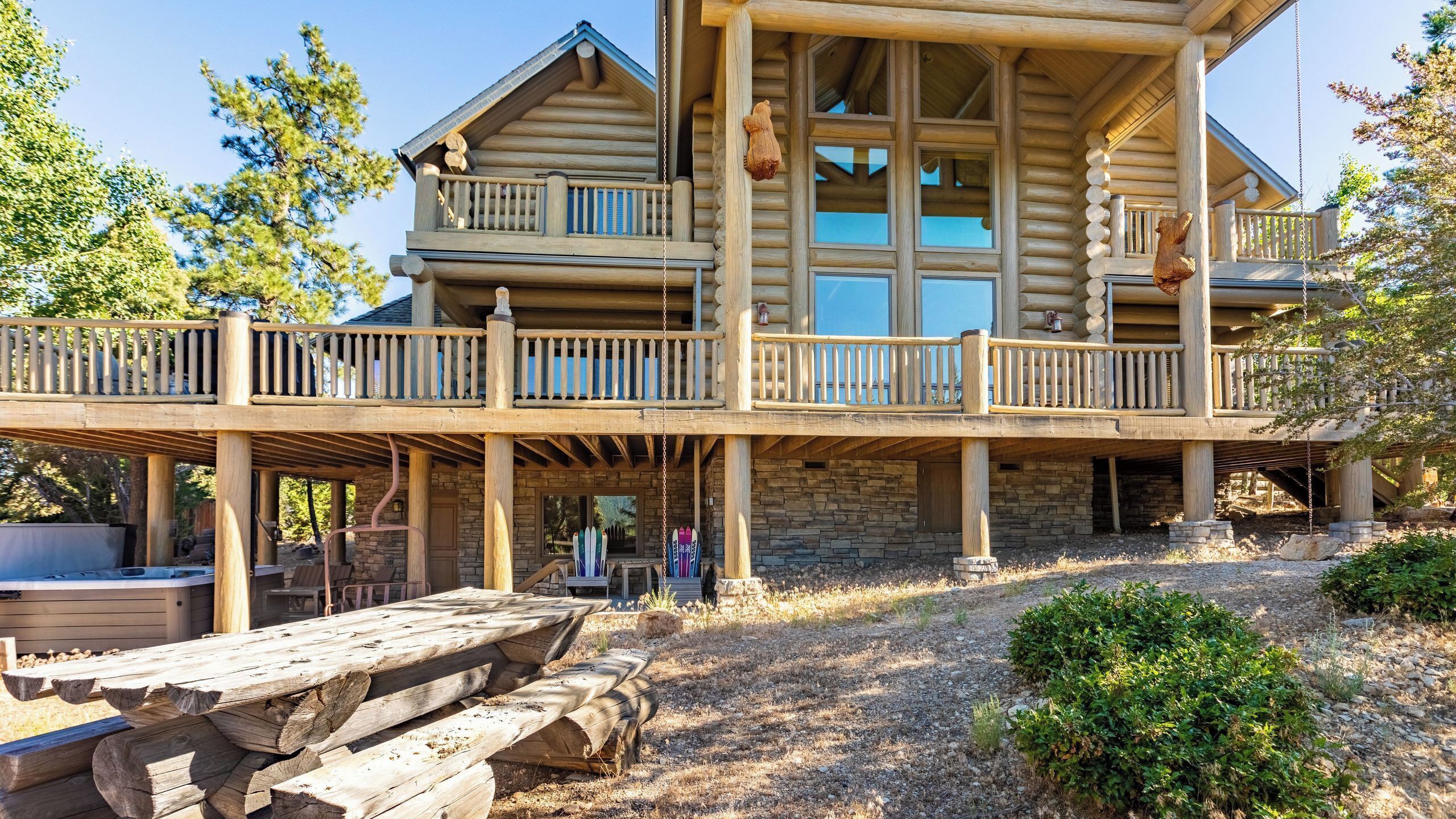 A log cabin with a balcony, outdoor seating, and a stone foundation.