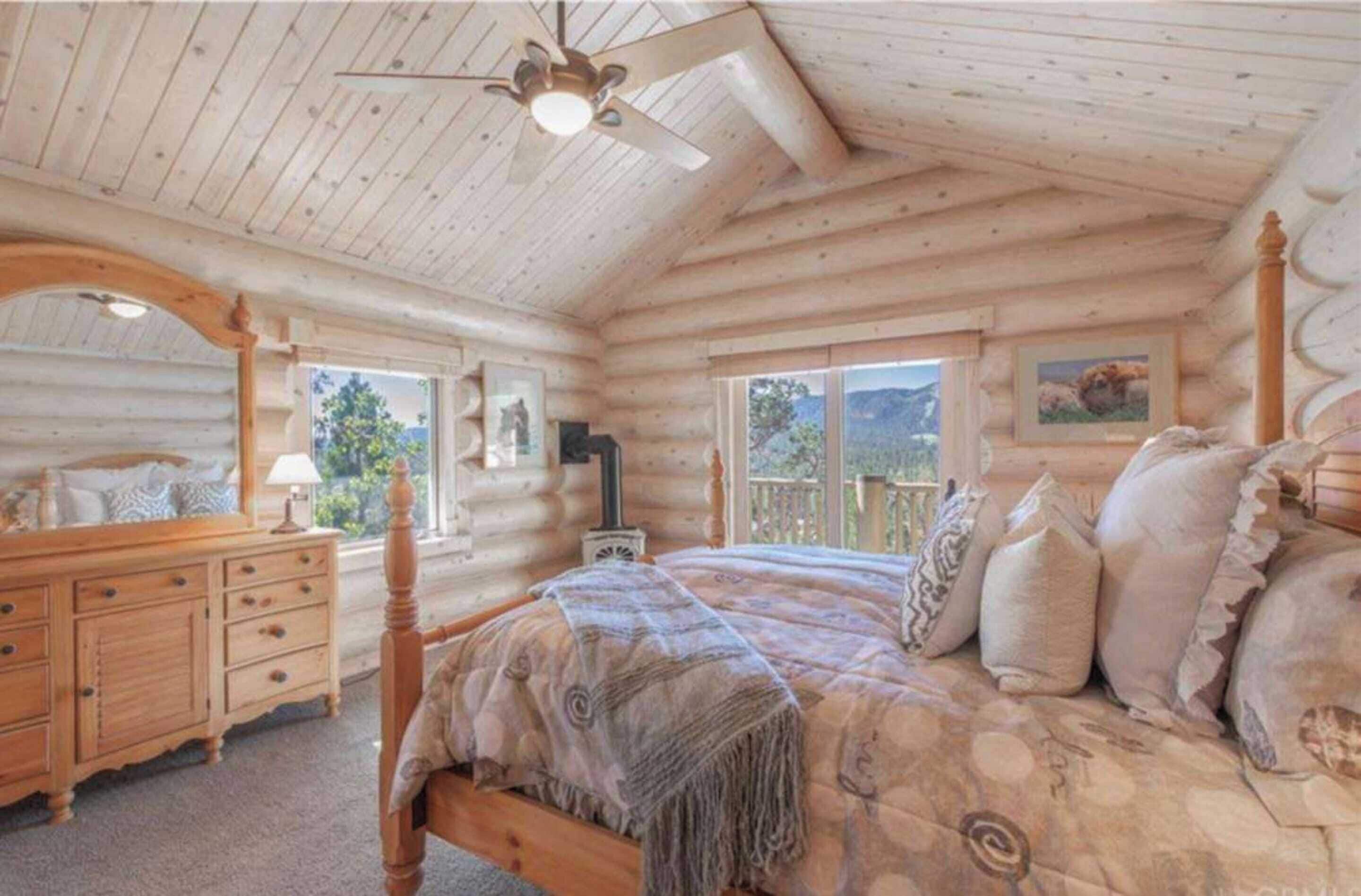 Een slaapkamer in een blokhut met een bed, een houten dressoir en een plafondventilator.