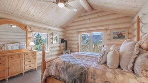 A log cabin bedroom with a bed, dresser, and a ceiling fan.