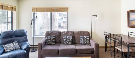 Una sala de estar con un sofá marrón, un sillón de cuero negro, una mesa de centro de madera y una mesa de comedor con sillas.