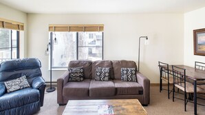 Un salon avec un canapé marron, un fauteuil en cuir noir, une table basse en bois et une table à manger avec des chaises.