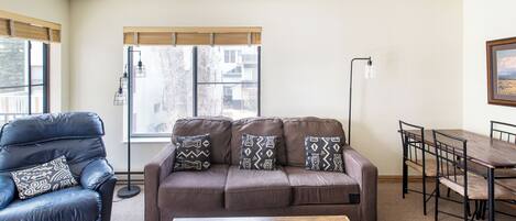 Una sala de estar con un sofá marrón, un sillón de cuero negro, una mesa de centro de madera y una mesa de comedor con sillas.