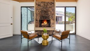 Un salon moderne avec une cheminée en pierre, des fauteuils en cuir et une vue sur l’extérieur.
