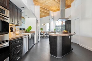A modern kitchen with dark wood cabinets, stainless steel appliances, and a central island. - El Reino by Avantstay Spectacular Estate w/ Pool & Tennis Court! (Palm Springs)