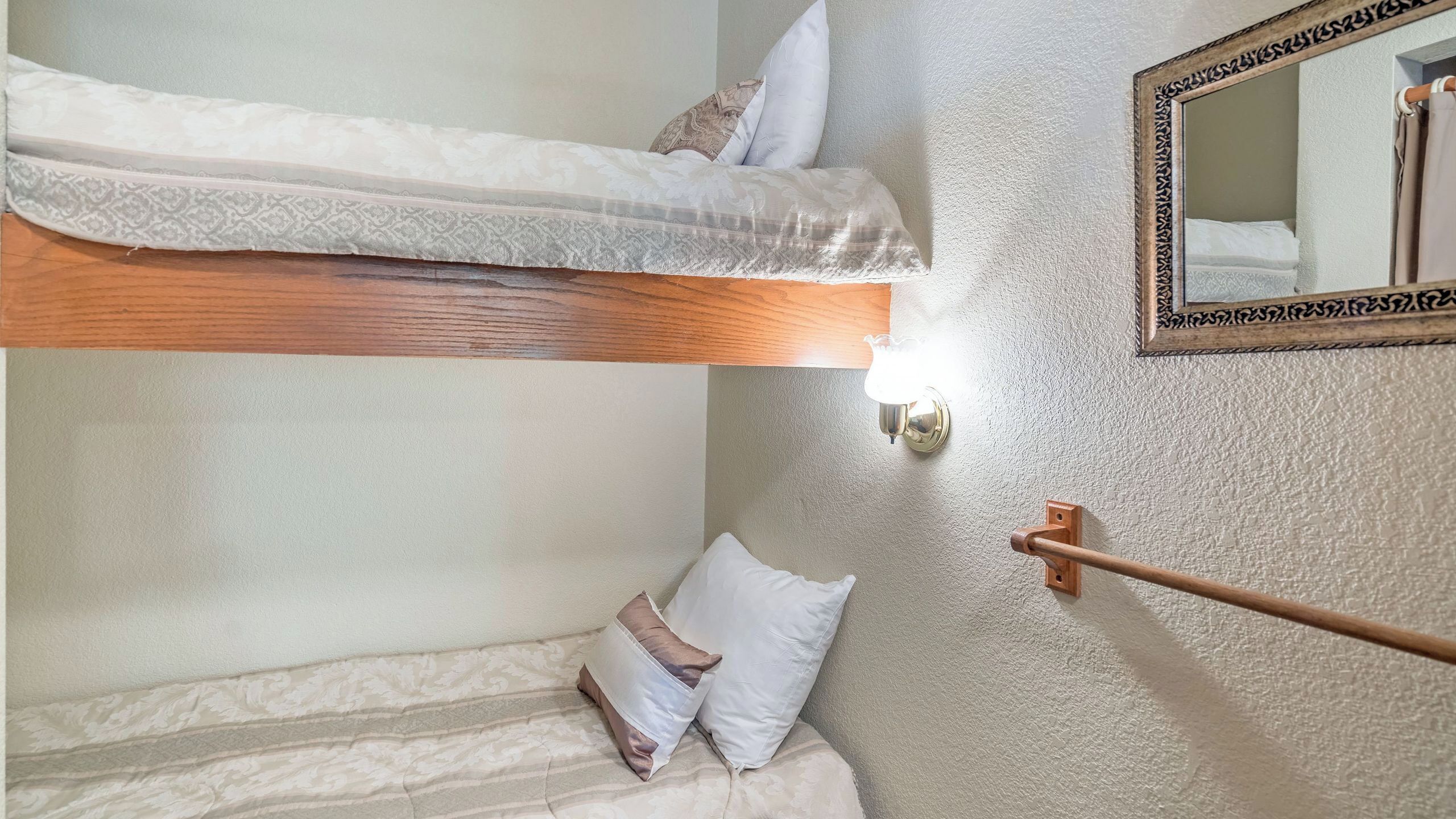 Een stapelbed met houten frame, een nachtkastje met lamp en een spiegel aan de muur.