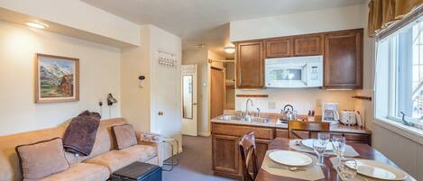 A compact kitchen with wooden cabinets, a microwave, and a dining area with a table set for four.