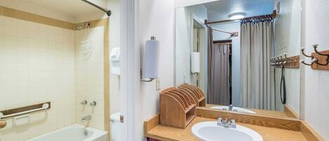 A bathroom with a bathtub, toilet, and wooden vanity with two sinks.