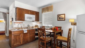 Cocina compacta con armarios de madera, un microondas, un fregadero y una zona de comedor con sillas.
