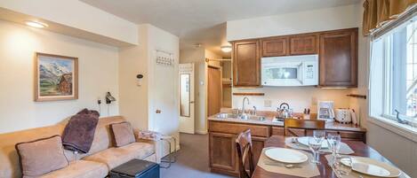 Een gezellige, compacte leefruimte met een kitchenette, een eethoek en een bank met een plaid.