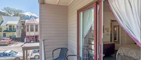 A balcony with two wicker chairs, a sliding glass door, and a view of a mountain.