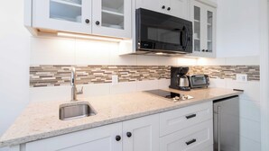 Una cocina moderna con armarios blancos, un microondas negro, un lavamanos de acero inoxidable y un salpicadero de azulejos.