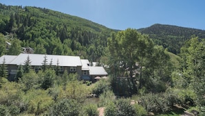 Un refugio de montaña con techo metálico, rodeado de bosque denso y colinas.