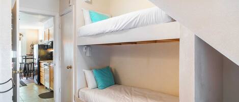 A bunk bed room with a kitchen area visible through an open door.