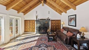 Ein geräumiges Wohnzimmer mit hohen Holzbalkendecken, einem Kamin, einem Ledersofa und einem großen Teppich mit Muster.