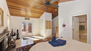 Ein Schlafzimmer mit Bett, Deckenventilator, Kamin, Fenster und einer Tür zu einem Badezimmer.
