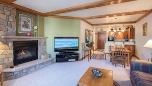 A living room with a stone fireplace, a television, and a dining area with wooden furniture.