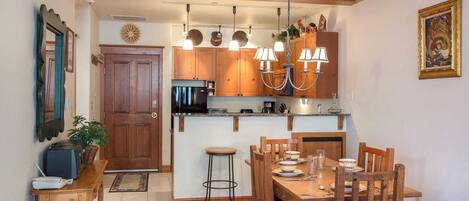 A compact kitchen with wooden cabinets, a built-in microwave, and a dining area with a wooden table and chairs.