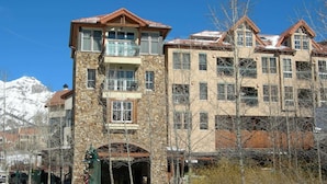 A multi-story hotel with stone facade, balconies, and a ski resort backdrop.